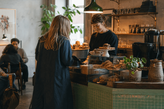 Kassadisk på ett oberoende kafé med kaffebryggare och en handskriven skylt om veckans bakverk